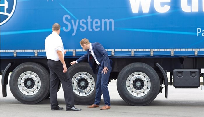 Two people standing next to a lorry and pointing towards the trailer suspension