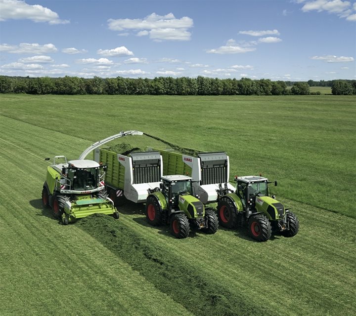 Two tractors dragging trailers while filling them with green waste