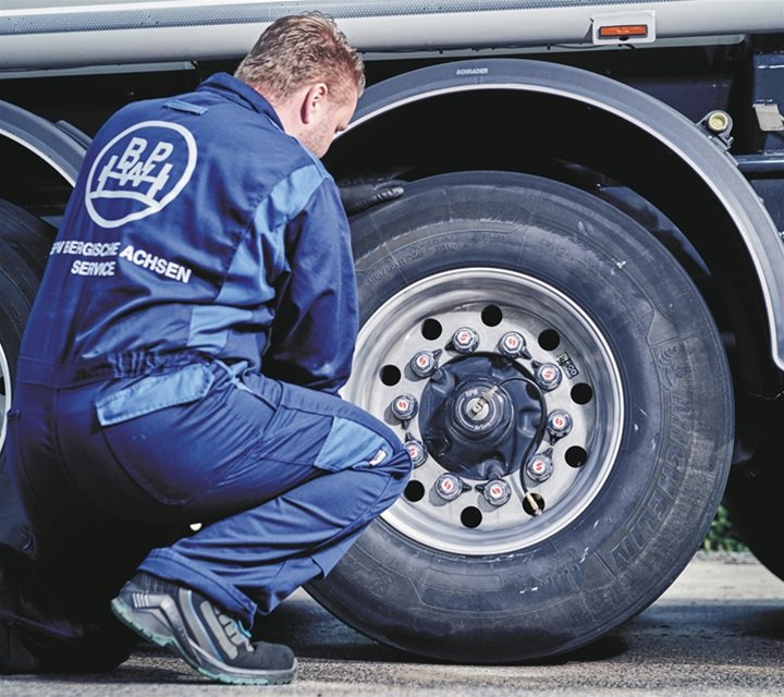 A mechanic kneeling next to a wheel 