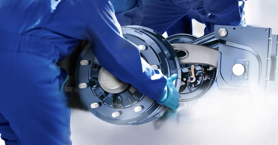 Three people in blue clothes installing a disc brake to the other vehicle components
